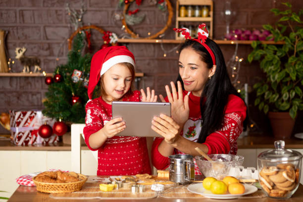 istock mom and daughter are talking via video link, passing greetings on a tablet in a dark kitchen with a Christmas tree for New Year or Christmas, smiling and having fun together in a Santa Claus hat 1473123776