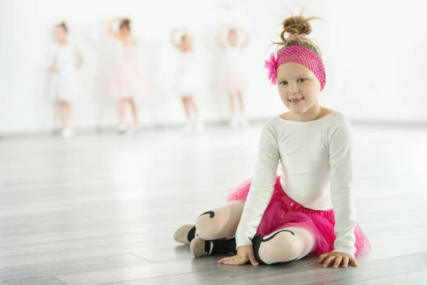 Closeup front view of elementary age girls in a ballet class sitting on floor and looking at the camera.
