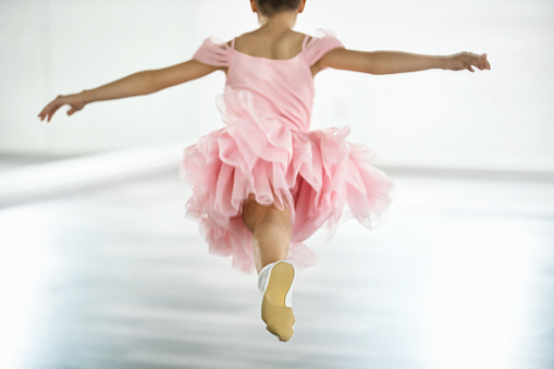 Closeup rear view of elementary age girl practicing ballet moves in front of a mirror at dance school.