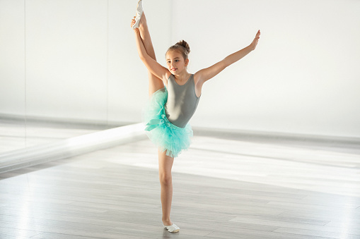 Closeup side view of elementary age girl practicing ballet moves in front of a mirror at dance school.