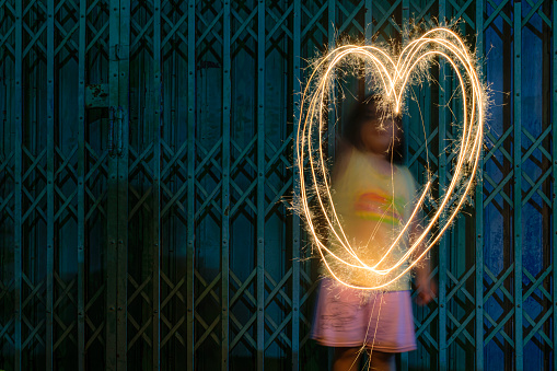 Girl draws out a heart using a sparkler on Bonfire night in Thailand. A large heart drawn out with a sparkler