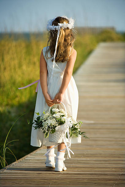 Flower Girl on Boardwalk Rear view of a flower girl walking on a boardwalk holding a flower basket behind her back. Vertical shot. flower girl stock pictures, royalty-free photos & images