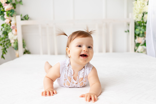 funny baby girl six months crawling in a bright beautiful room on a white bed in a lace bodysuit and smiling