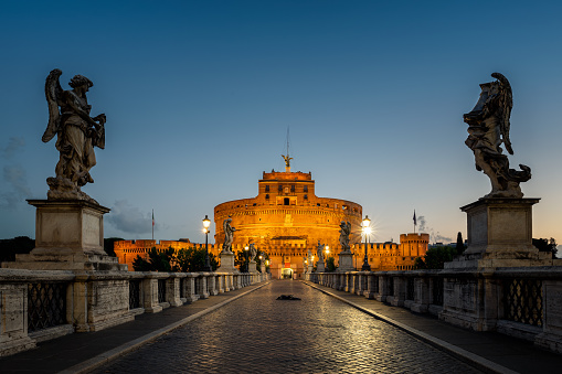 Rome - September 10, 2022: View of the illuminated Mausoleum of Hadrian, known as Castel Sant'Angelo from the Sant'Angelo bridge in blue hour before sunrise.