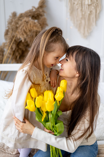 a little girl of a child with her mother hug and kiss giving a bouquet of yellow tulips. Lifestyle. Fresh flowers. International Women's Day or Mother's Day. High-quality photography