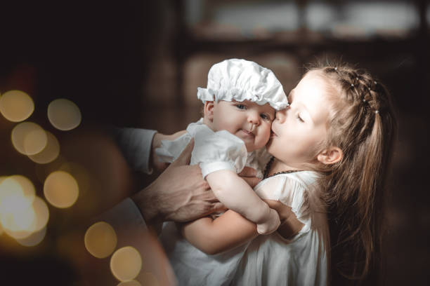 the elder sister kisses a baby in a baptismal outfit in a temple or church who came to worship in an orthodox church or baptism a baby - batismo imagens e fotografias de stock