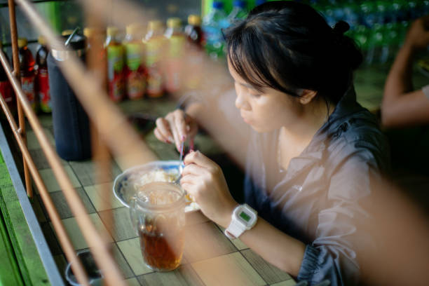 Asian Girl Eating In A Local Traditional Indonesian Food Stall Behind Steel Bars After Morning Walk stock photo