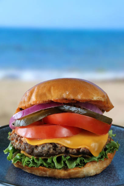 Close-up image of gourmet fast food takeaway double cheeseburger served in seedless burger bun, bacon, melted cheese, tomatoes, lettuce and onion, focus on foreground