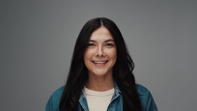 Portrait of Young Woman Looking at Camera in Colour Studio Shot. Happy Adult Female Isolated Alone on Grey Background Close-up. Multiracial Person with Gorgeous Face Opening Dark Eyes Smiling Bright