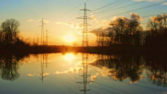 AERIAL Stunning sunset footage of electric pylons with reflection in lake
