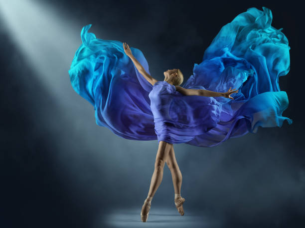 bailarina en vestido de gasa púrpura en el haz de luz del escenario. bailarina de ballet con vestido azul fantasía de seda. mujer bailando con tela cian voladora como alas sobre fondo oscuro - ballet dress studio shot costume fotografías e imágenes de stock