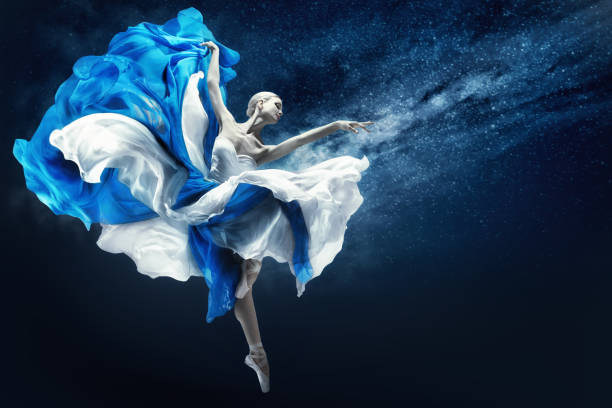 Ballerina dancing in Blue Chiffon Dress over Night Sky Background. Ballet Dancer jumping in fluttering Skirt pointing towards Hand. Fantasy Woman as Antique Goddess stock photo