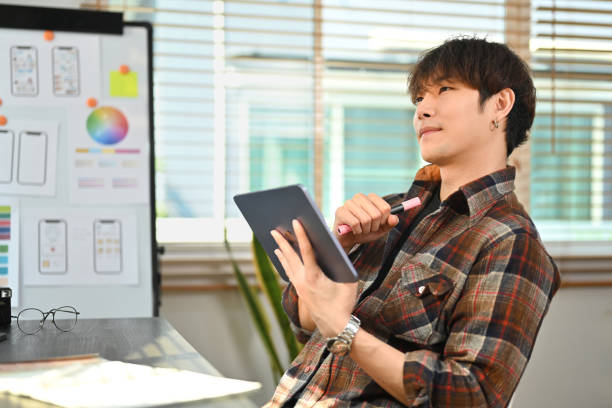 istock Thoughtful asian man UX graphic designer sitting at creative workplace and contemplating new project idea. 1473137969
