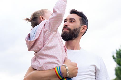 Father with a rainbow lgbt bracelet holding a little girl outdoors
