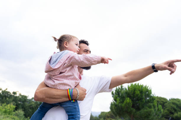 Father with lgbt bracelet pointing ahead holding a little girl stock photo