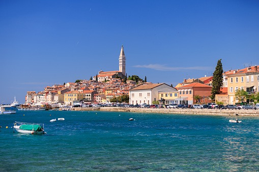 View across the sea surface on the town of Rovinj on the hill with Church of St. Euphemia tower on top, boats anchored