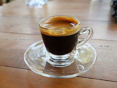 Hot Espresso Coffee in a transparent glass cup with crema on wooden table