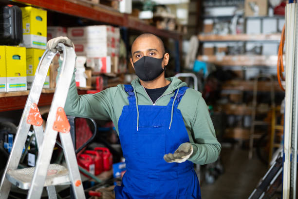 istock Warehouse worker in protective mask stands next to stepladder and tool shelves in hardware store 1473139429