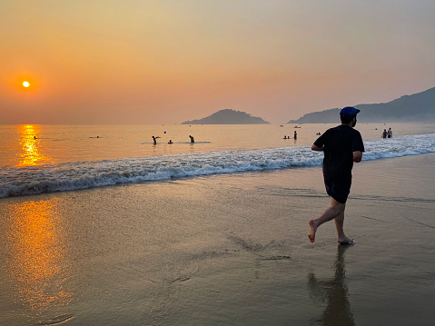Stock photo showing an Indian man on holiday in Goa, South India, pictured running on Palolem Beach, jogging in the gentle sea waves at sunset, a particularly popular winter holiday destination for both English and German tourists.
