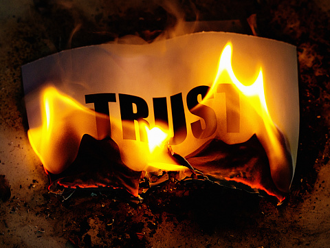The word TRUST printed in bold type, being consumed by fire.