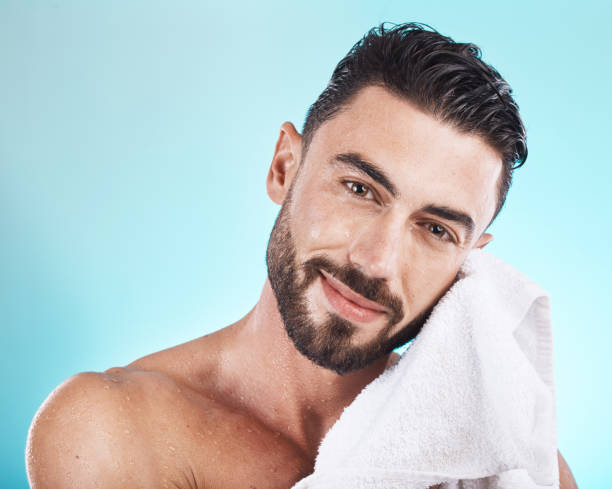 cara del hombre, toalla y cuidado de la piel mientras está mojado después de una ducha, facial o baño para el cuidado de la piel, la higiene y la dermatología en azul. retrato de modelo masculino feliz en estudio para un cuerpo limpio para la salud y e - male towel men human face fotografías e imágenes de stock