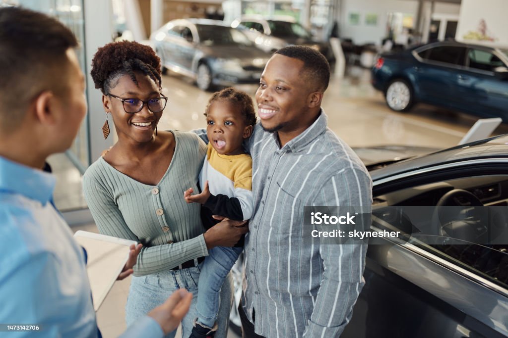 Happy black family talking to car salesperson in a showroom. Happy African American family communicating with male salesperson in a car showroom. Car Stock Photo