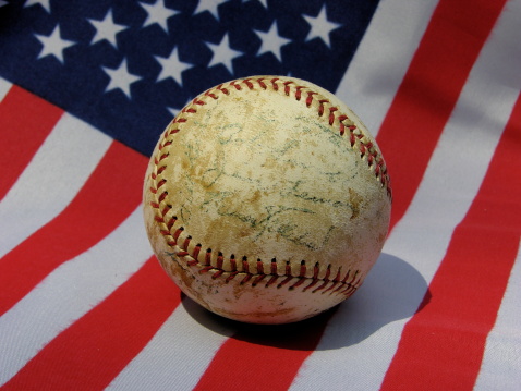 Old, worn baseball with faded autographs on USA flag. Image taken in afternoon summer sun.