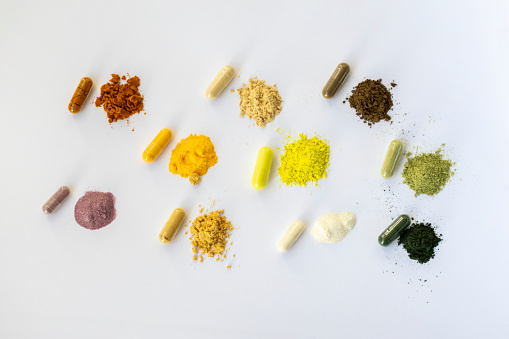 Opened and whole capsules of supplements on white background. Various pills and vitamins. From top right to left as follows: curcumin, vitamin C, ant tree bark, quercetin, q10, vegetable supplement, resveratrol, ginger, enzymes, spirulina
