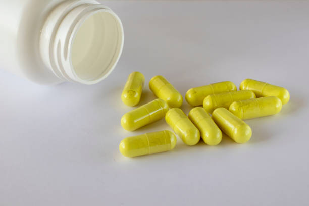栄養補助食品の瓶は、白い背景に振りかけられた黄色のケルセチンカプセルの隣にあります。 - quercetin ストックフォトと画像