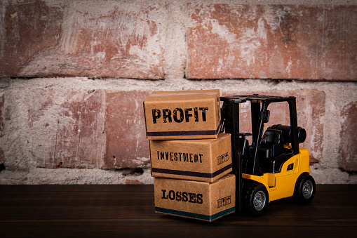 PROFIT LOSS INVESTMENT Concept. Miniature cardboard boxes on a wood and brick background.
