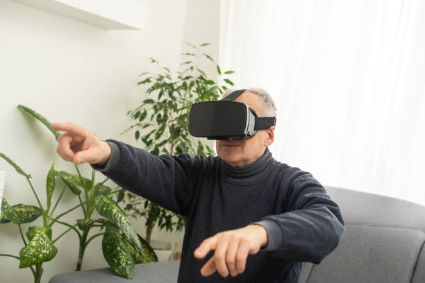 istock handsome senior man using VR 360 glasses at home. Making browse and tap gestures. Concept of active modern elderly people, learning to use contemporary technologies. 1473146505