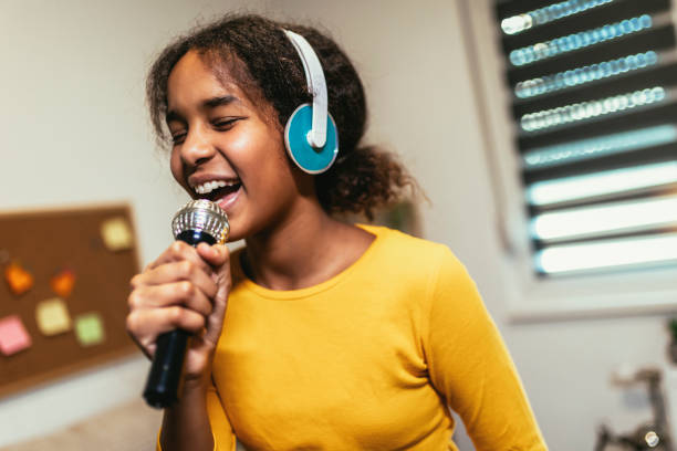 Black girl  holding microphon singing karaoke at home, recording songs for contest.