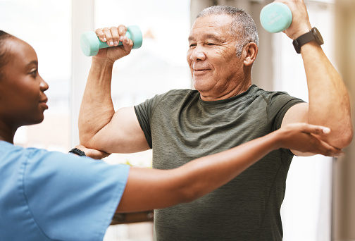 Medical, training and physiotherapy with dumbbell and old man with nurse for rehabilitation, support and retirement. Healthcare, help and physical therapy with patient and black woman in nursing home