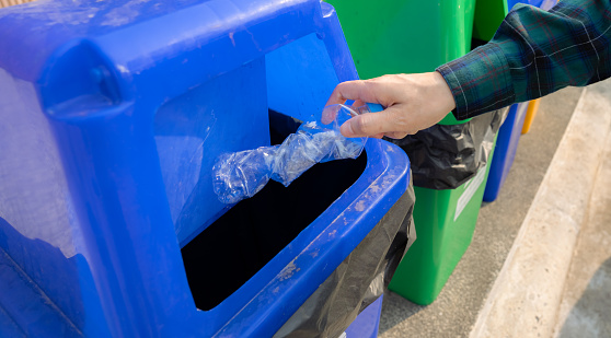 People hand throwing empty water bottle in recycle bin. Blue plastic recycle bin. Man discard water bottle in trash bin. Waste management. Plastic bottle garbage. Reduce and reuse plastic concept.