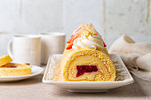 Swiss or jelly roll cake, roulade or Swiss log. Rolled sponge cake filled with custard cream and berry jelly, decorated with whipped cream cheese and strawberries.