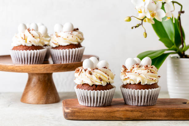 istock Easter table with chocolate cupcakes, sweet candy eggs and cream cheese nest. Spring white flowers. Holiday homemade dessert. 1473151615