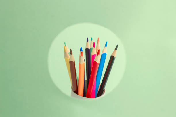 um conjunto de lápis de cor espreita de um círculo rosa sobre um fundo verde. conceito de lápis afiados - material variation timber stacking - fotografias e filmes do acervo