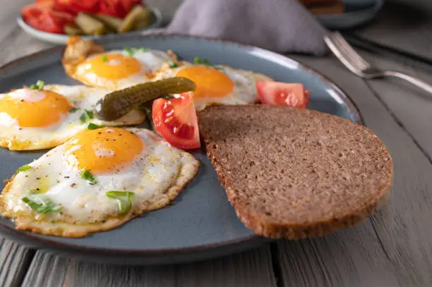 Homemade fresh pan fried eggs, sunny side up. Served with rye bread, tomatoes and pickles on a plate. Traditional german, rustic meal for breadfast, lunch or dinner. Closeup, front view