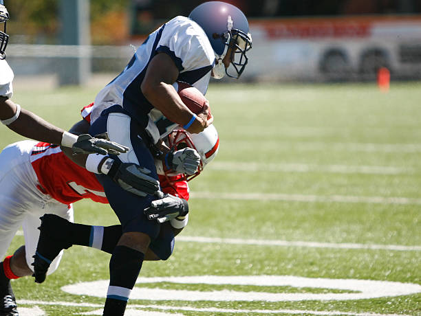 College Football Tackle College football game.  The running back bursts through an opening in the line.  A diving tackle is all that stops him from scoring a touchdown. wide receiver athlete stock pictures, royalty-free photos & images