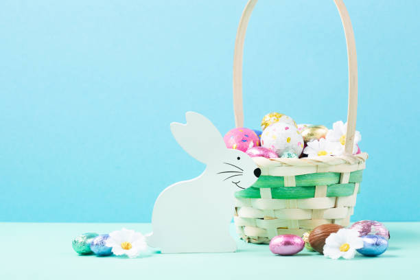 istock Easter Basket, Sweet Colorful Chocolate Easter Eggs, Daisy Flowers on Pastel Blue Mint Background. 1473157436