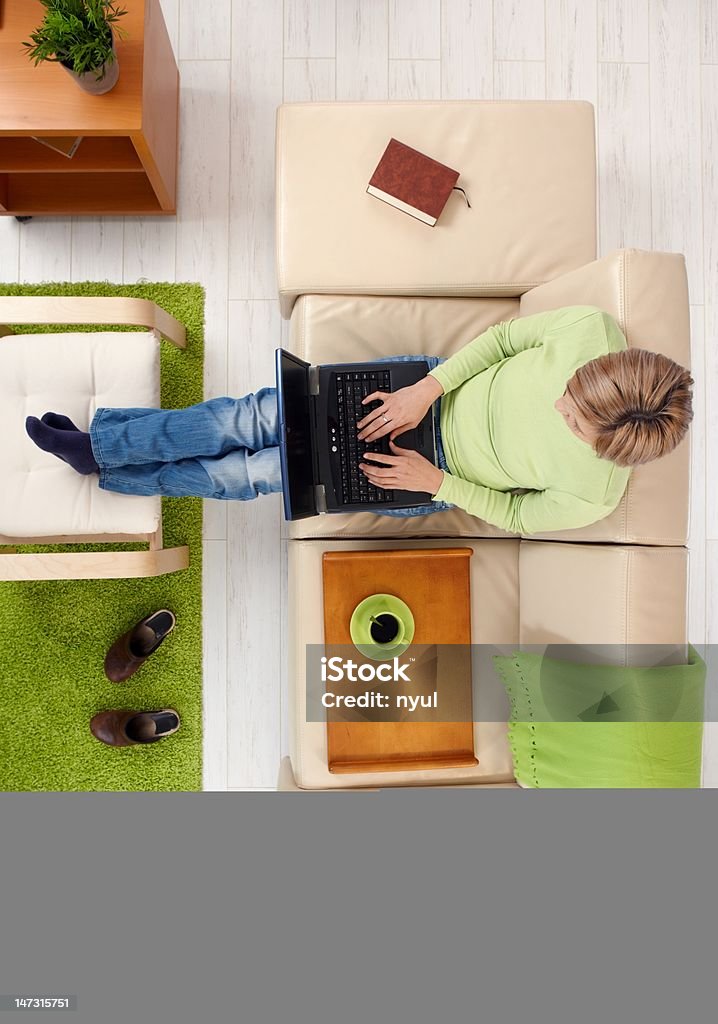 Woman with laptop from above Woman typing on laptop keyboard sitting on sofa with legs crossed on footboard in high angle view. 20-29 Years Stock Photo