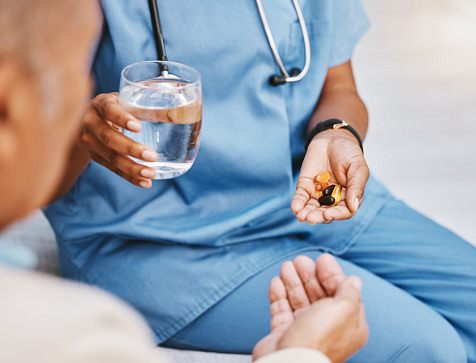 Pills, water and hands of nurse with patient in nursing home for wellness, healthcare and prescription. Doctor, medical care and health worker with vitamins, supplements and medication treatment