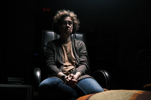 Mature woman sitting in the armchair in the dark room with her eyes closed