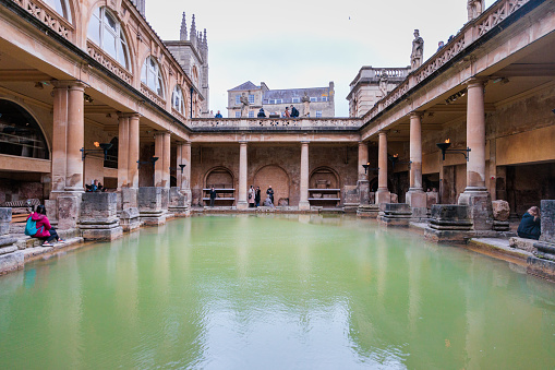 Tourist walking around the famous historical site, the Roman Baths, ancient architecture in England, UK