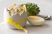 Vegetable salad with mayonnaise in eggshell shaped bowl, egg and cress, easter food concept