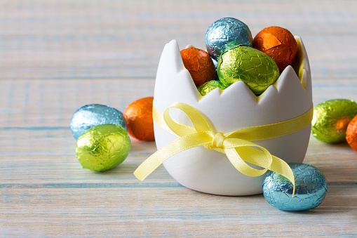 Chocolate easter egg in eggshell shaped bowl on light wooden background, easter sweets, decoration concept