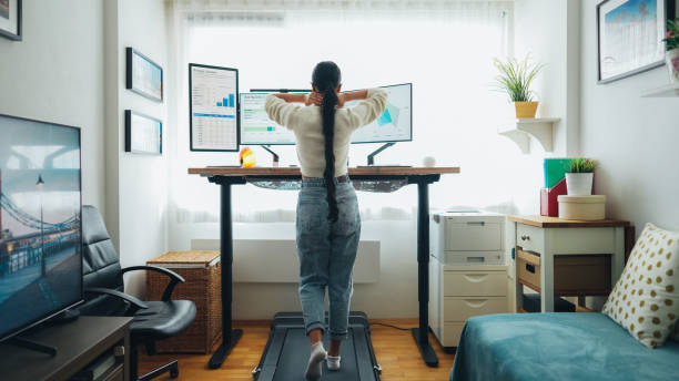 Woman at home office is walking on under desk treadmill Woman working from home at standing desk is walking on under desk treadmill treadmill stock pictures, royalty-free photos & images