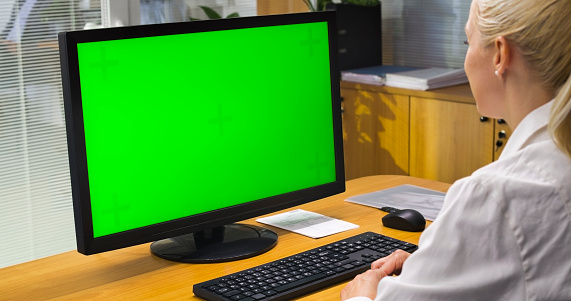 Female doctor looking at green screen of computer in office.