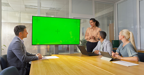Businesswoman discussing with colleagues during presentation off green screen in office.