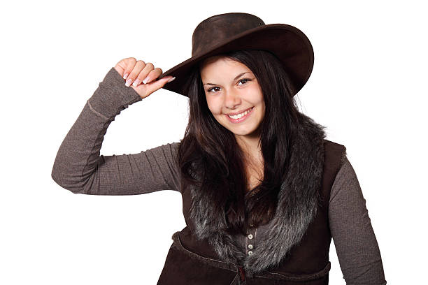 An attractive cowgirl standing isolated on gray while pointing her pistol